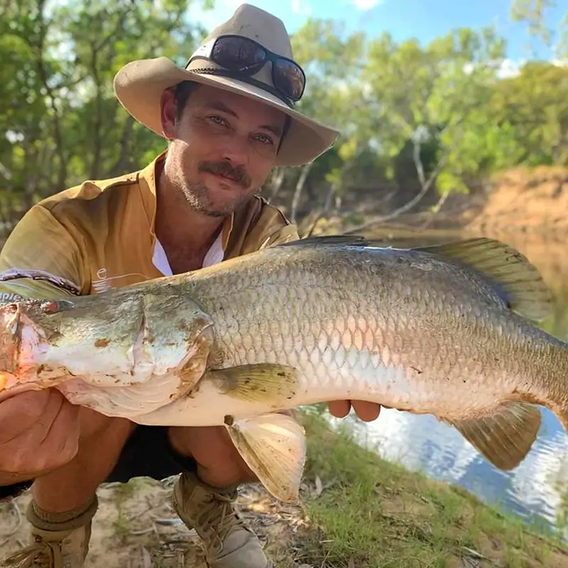 Fisher showing off a barramundi caught in shallow, shaded waters.