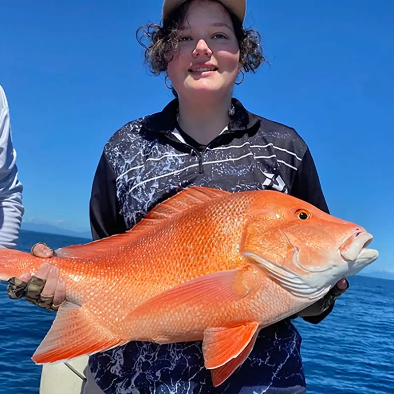 Smiling fisher holding a vibrant coral trout, against a sunny ocean backdrop.